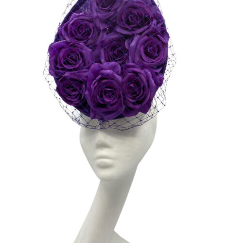 Cadbury purple coloured percher hat with purple roses in the centre and finished with a purple netting over the headpiece.